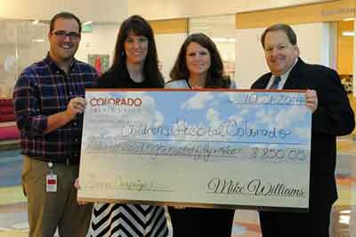 4 people smiling and holding a check for $8,850.05 that is being donated to the Children's Hospital of Colorado